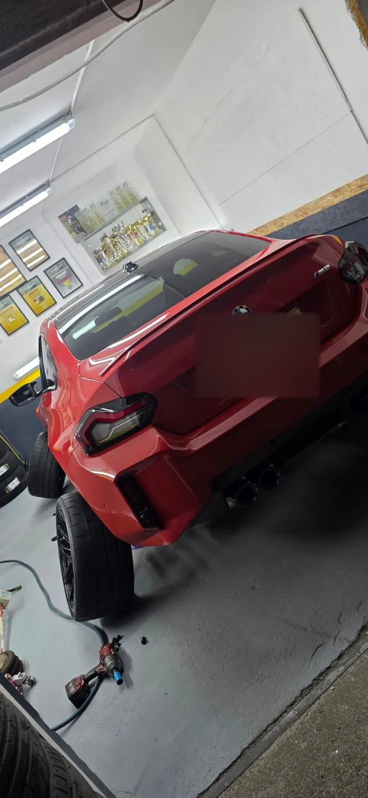 Crveni BMW M2 podignut na dizalici, bez stražnjeg kotača